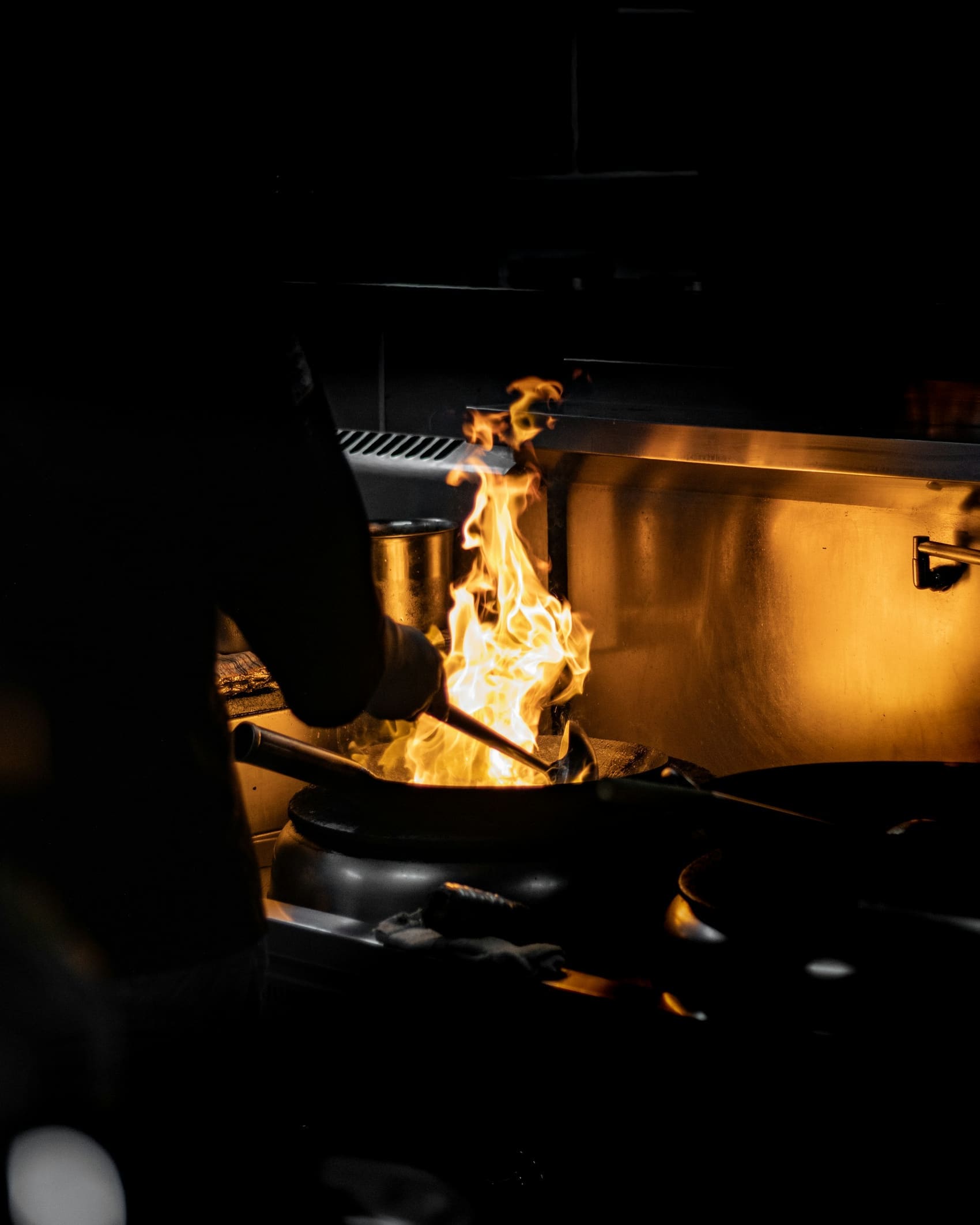 Flame rising from a pan on the grill in a dark kitchen, copper catching the light