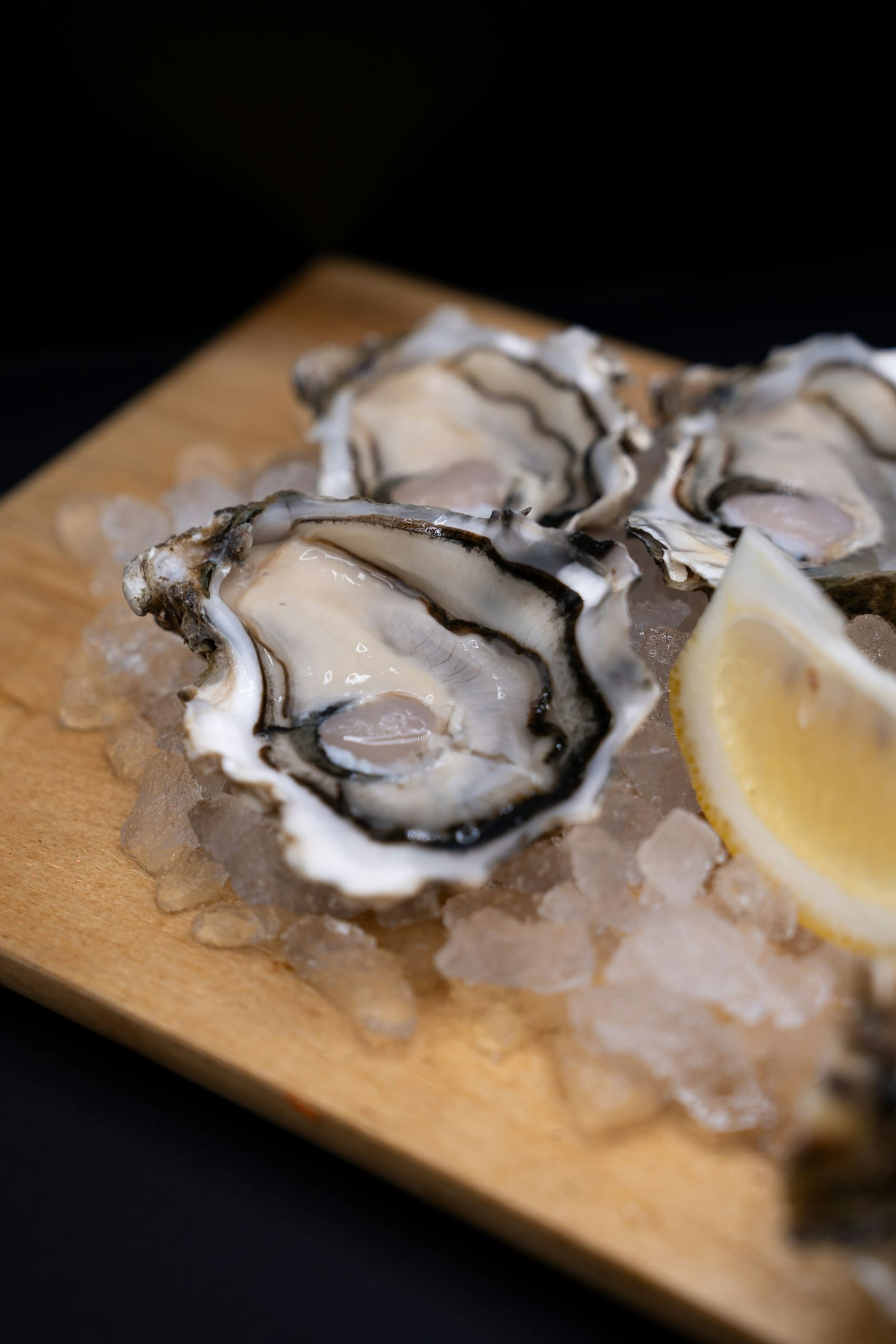 Freshly opened oysters resting on crushed ice on a wooden board