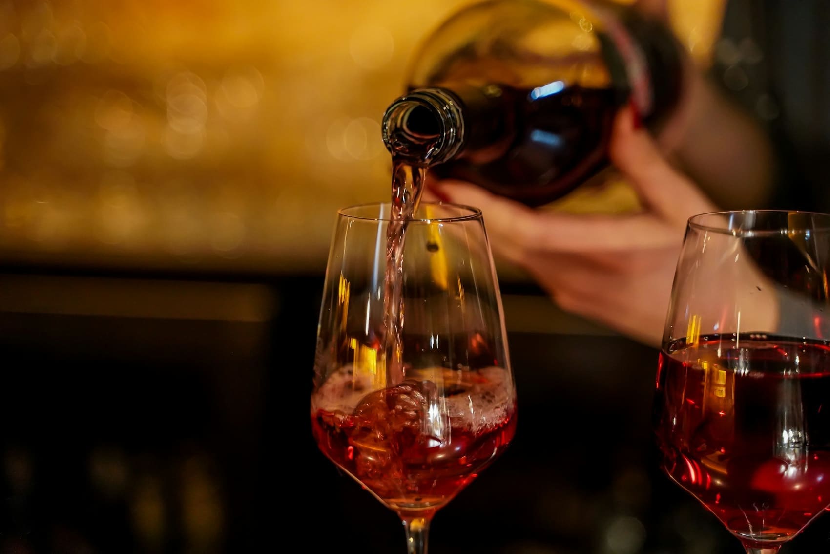 Red wine being poured into a glass at the bar, warm light behind